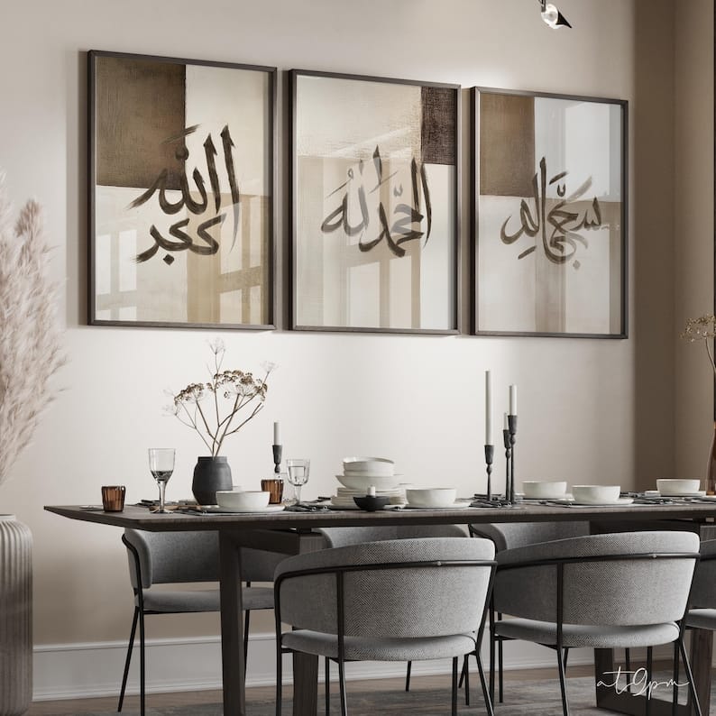 Dining room with a long table set for dinner, gray chairs, and wall art with Arabic calligraphy.