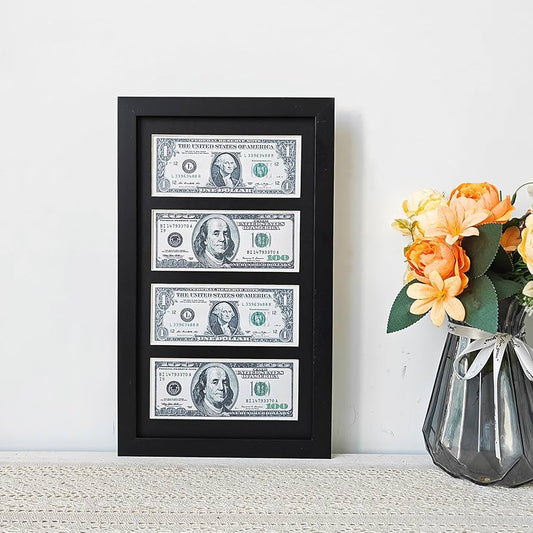 A black-framed wall art featuring realistic US dollar currency prints, placed on a table beside a flower vase.