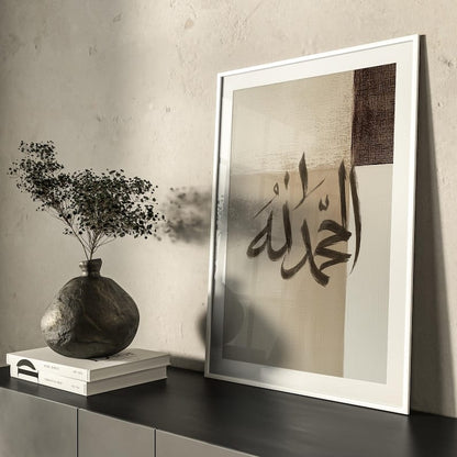 Framed artwork with Arabic calligraphy on a wall with a vase and books below.